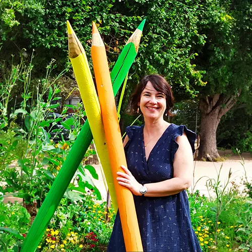 Graphopédagogue, à Roanne, posant devant de grands crayons colorés dans un jardin.